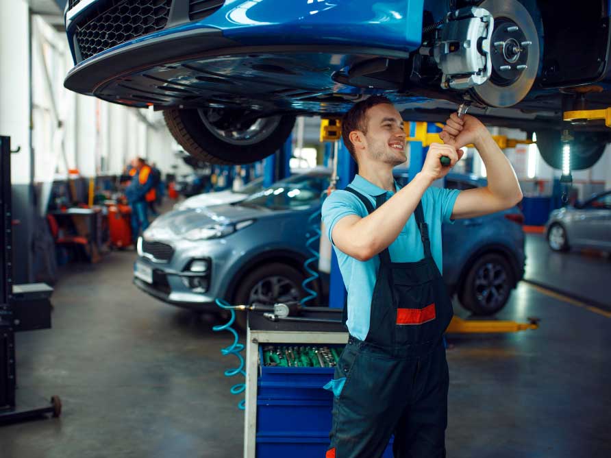 Professional auto technician performing undercarriage repair on vehicle in a modern service garage, showcasing expert Auto Body Shop Ft Lauderdale FL services for reliable collision repair and maintenance
