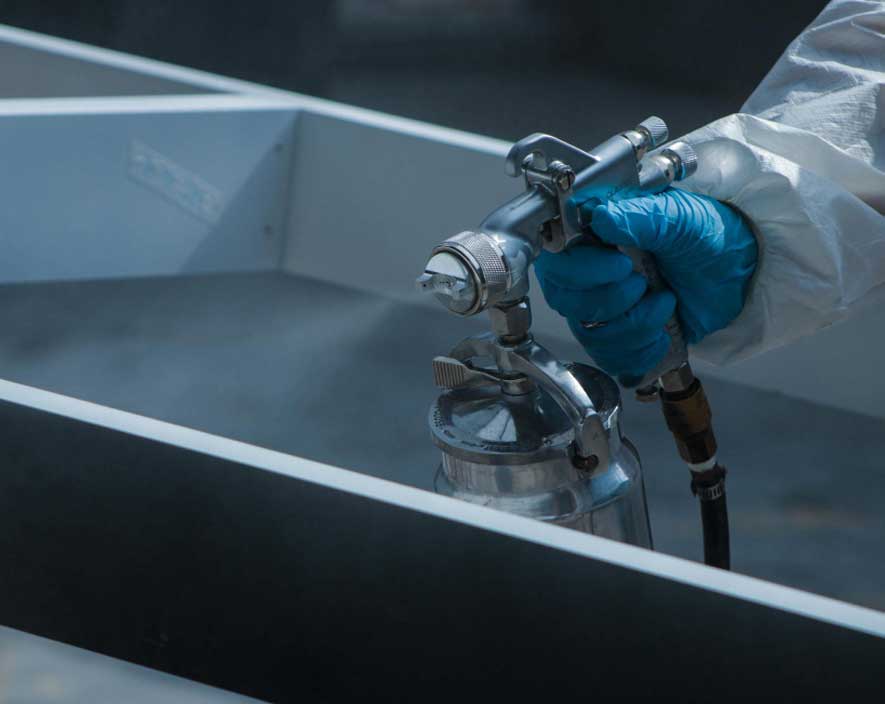 Close-up of a worker using a spray gun to coat metal surfaces with protective industrial paint, showcasing professional application by an Industrial Paint Supplier