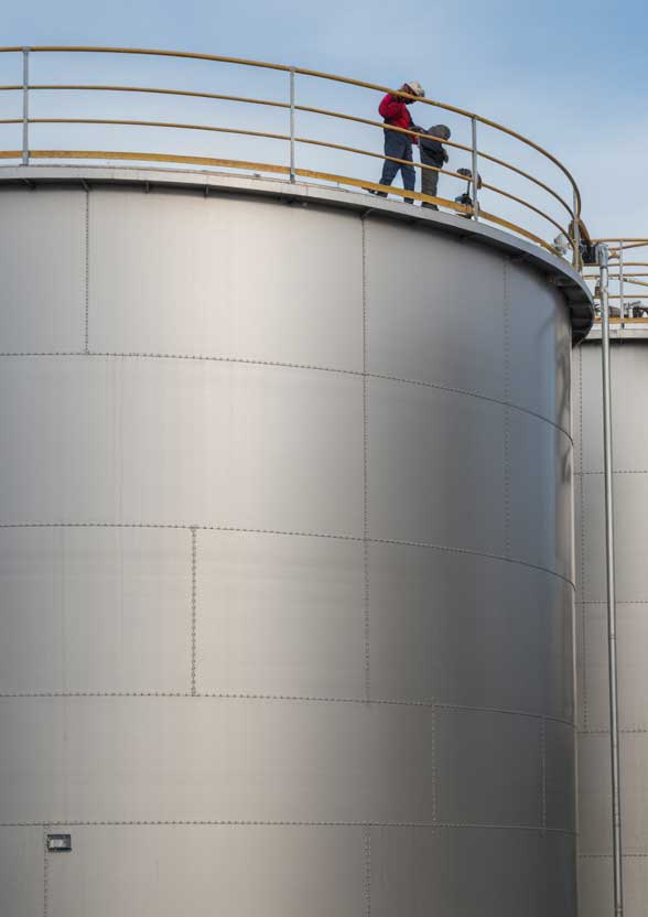 Industrial Sealant Supplier assisting with inspection and sealing maintenance on large metal storage tank at industrial facility.